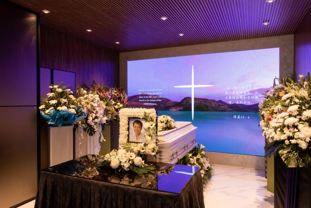 An elegant funeral parlour with a Christian funeral set up, featuring a casket adorned with floral arrangements